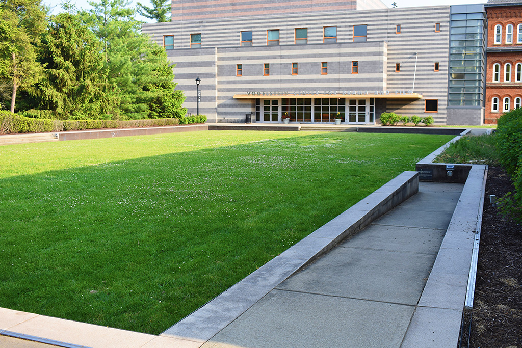 A long, recessed, green lawn with ramp access in each corner, bordered by bushes and trees.