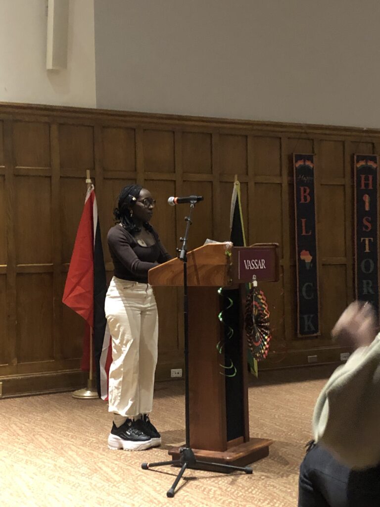 Shayasia Arnold standing at the podium reciting a poem into the mic for audience members. 