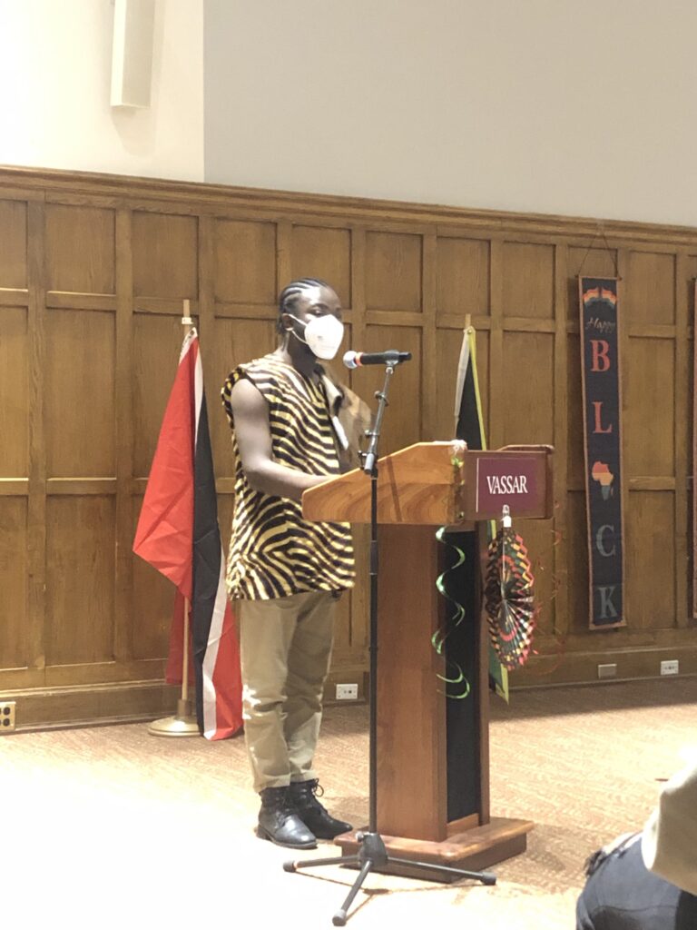 Favour Movel wearing a face mask, reciting a poem at the podium.