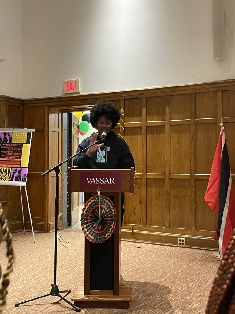 Carl Webster standing at the podium using the mic to introduce Faculty Speaker, Kimberly Williams Brown, 
Assistant Professor of Education. 