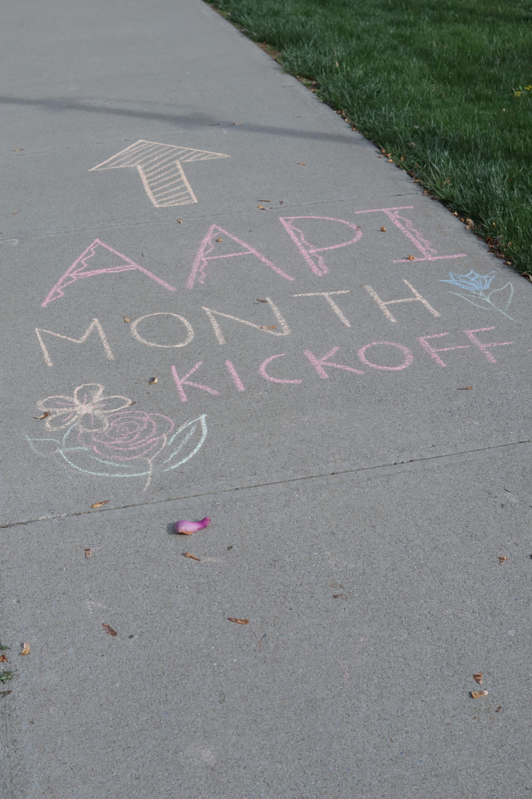 AAPI Month Kickoff displayed in colorful chalk writing on the sidewalk. Chalk flower artwork and letters written by Alysa Chen '23. 