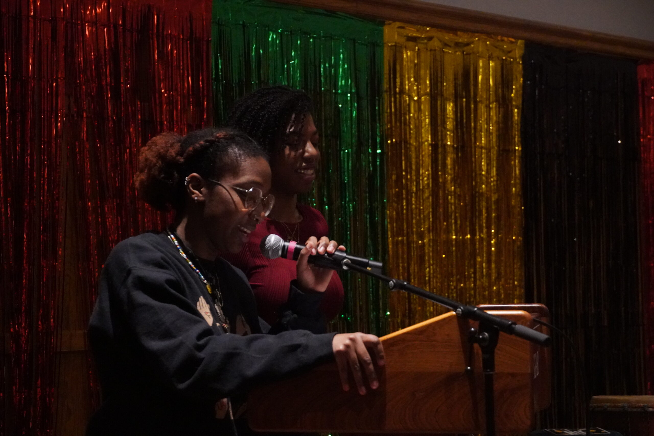 Mariah Jones and Marissa Desir standing at the podium. Mariah has her left hand on the mic and Marissa is standing next to Mariah on the left side. 