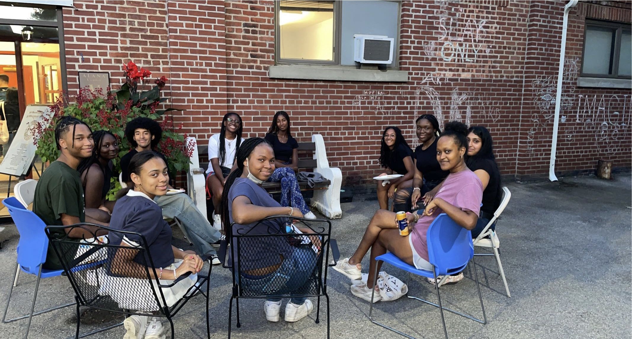 Group of eleven students seated outside in a circle of chairs.