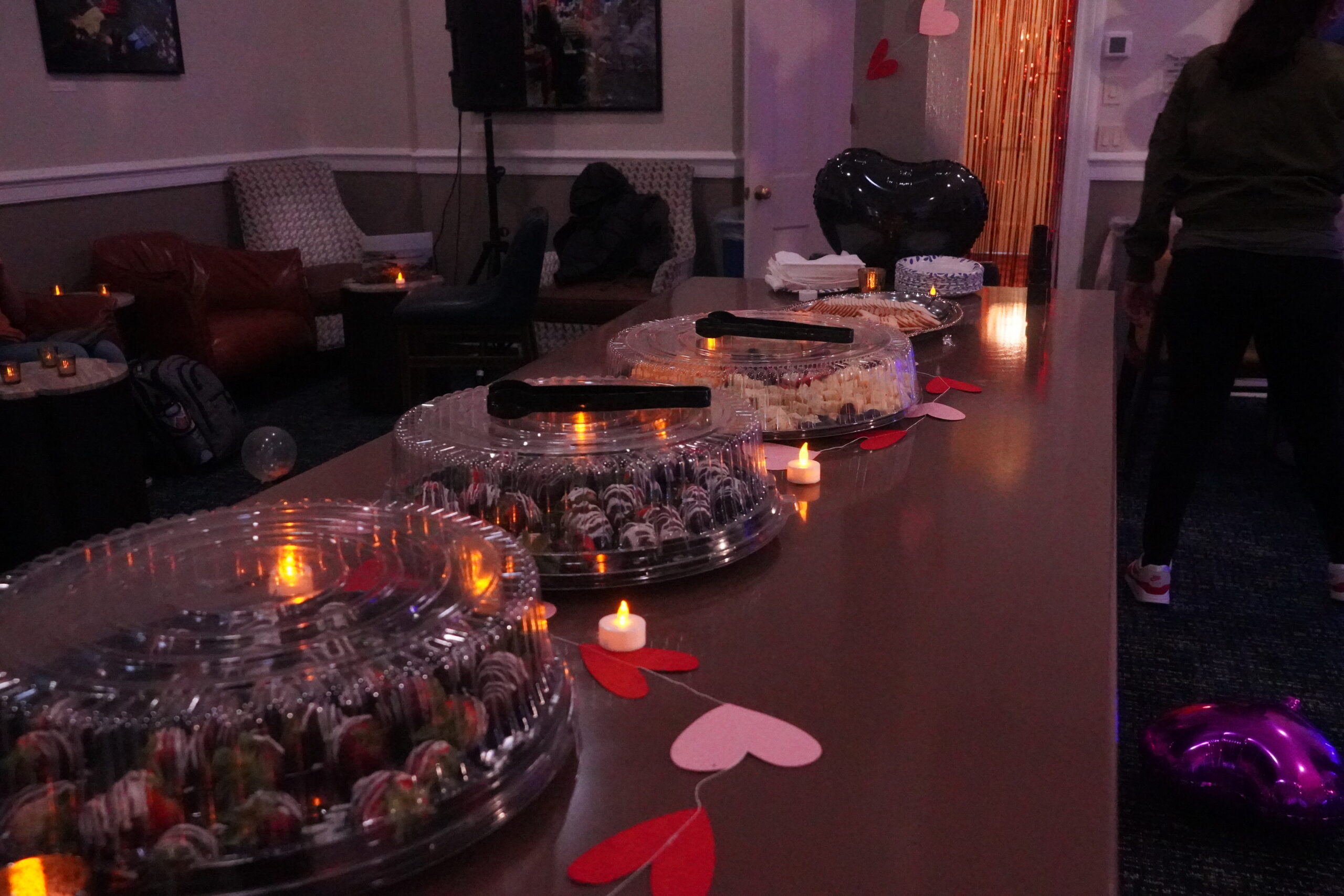 A table with trays of chocolate covered strawberries and pink and red paper hearts, and tealights.