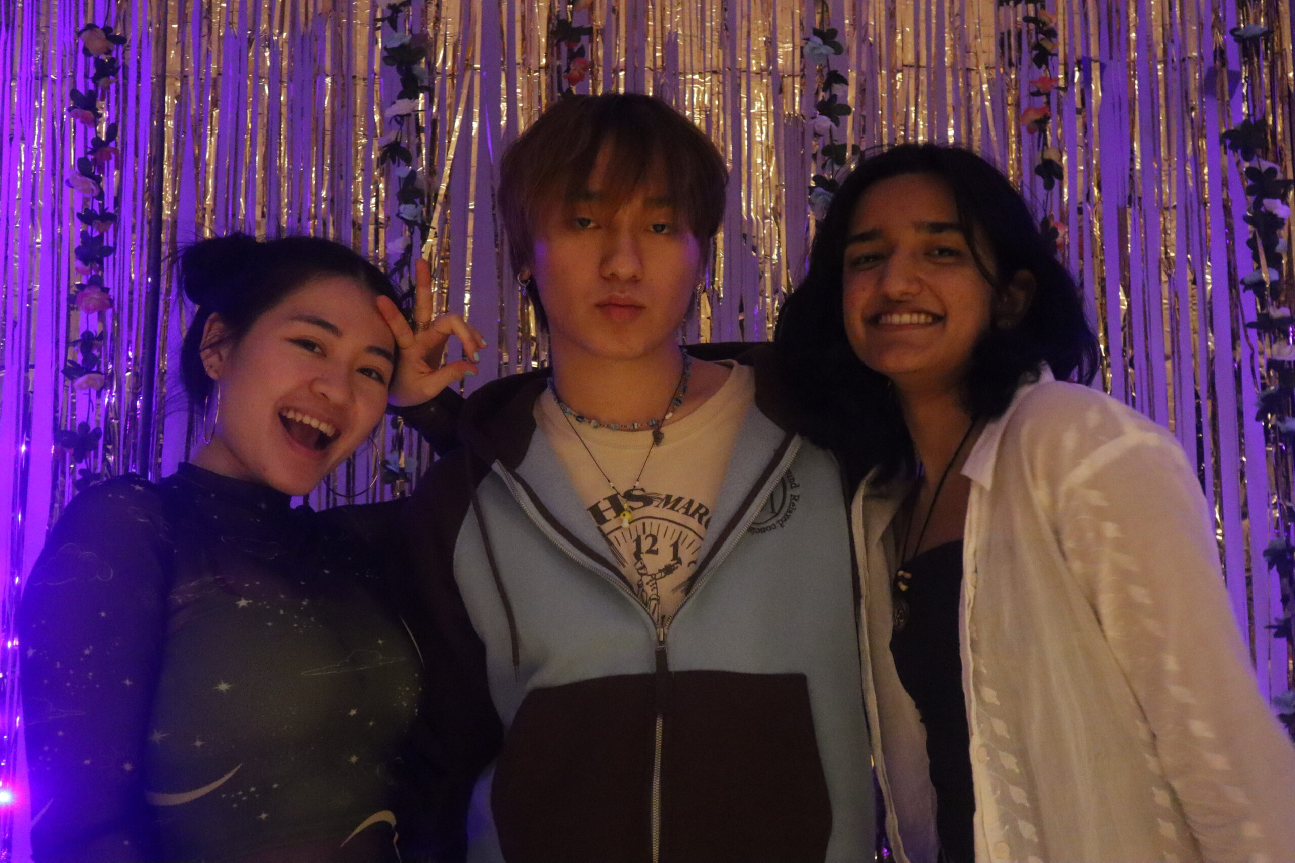 Three students standing side by side posing as they look into the camera and stand in front of the photo booth.