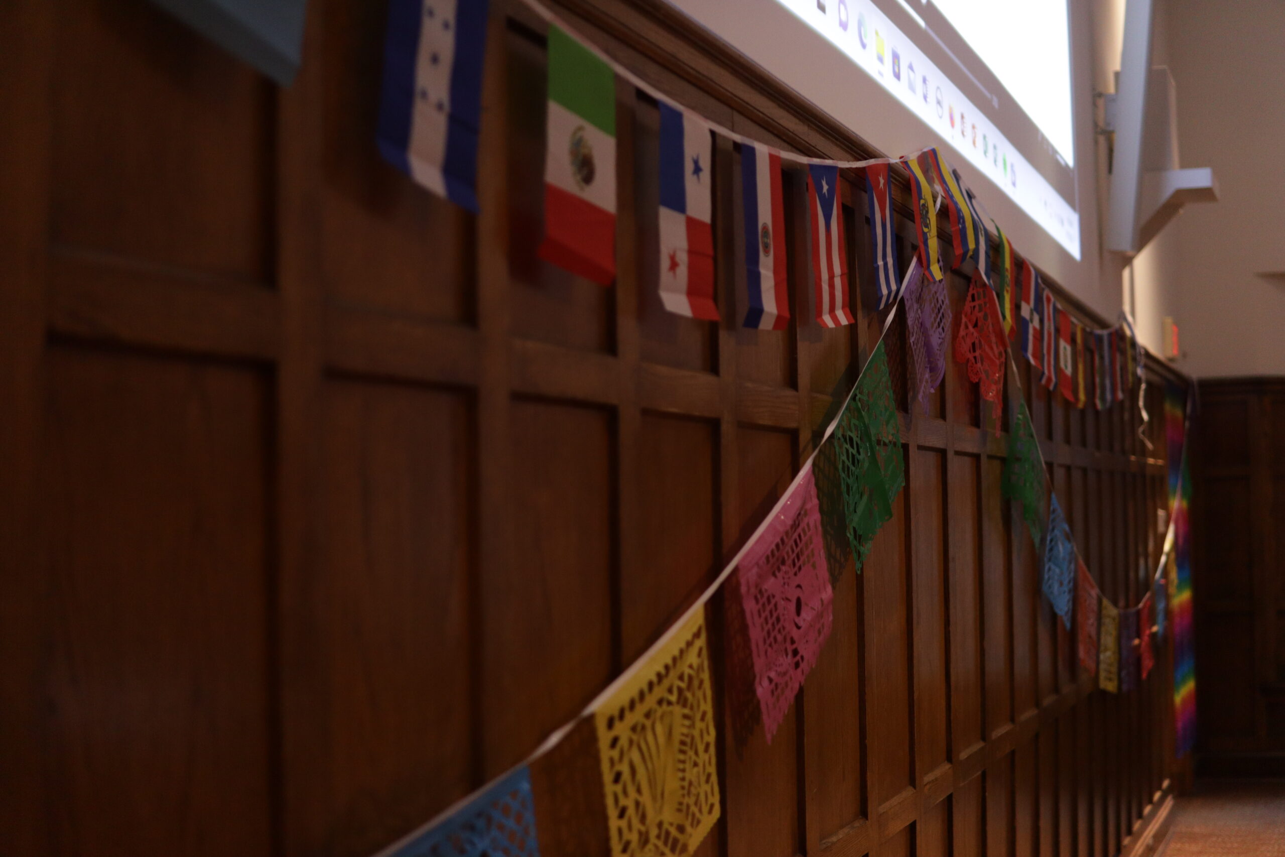 Flag banner with various flags and a Latin American patterned banner pictured as they are hung across the front of the Villard walls.