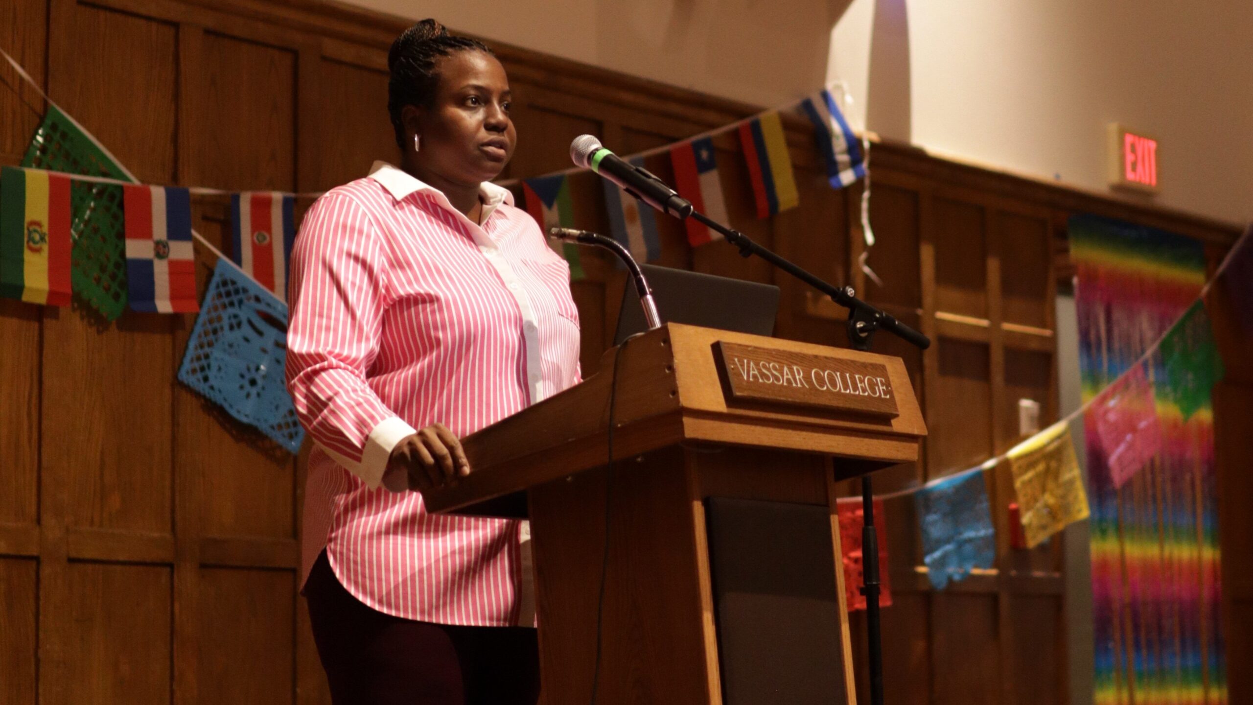 Nicole Beveridge standing in front of a brown podium with the words "Vassar College" on a maroon board and getting ready to speak into the mic attached to the podium.