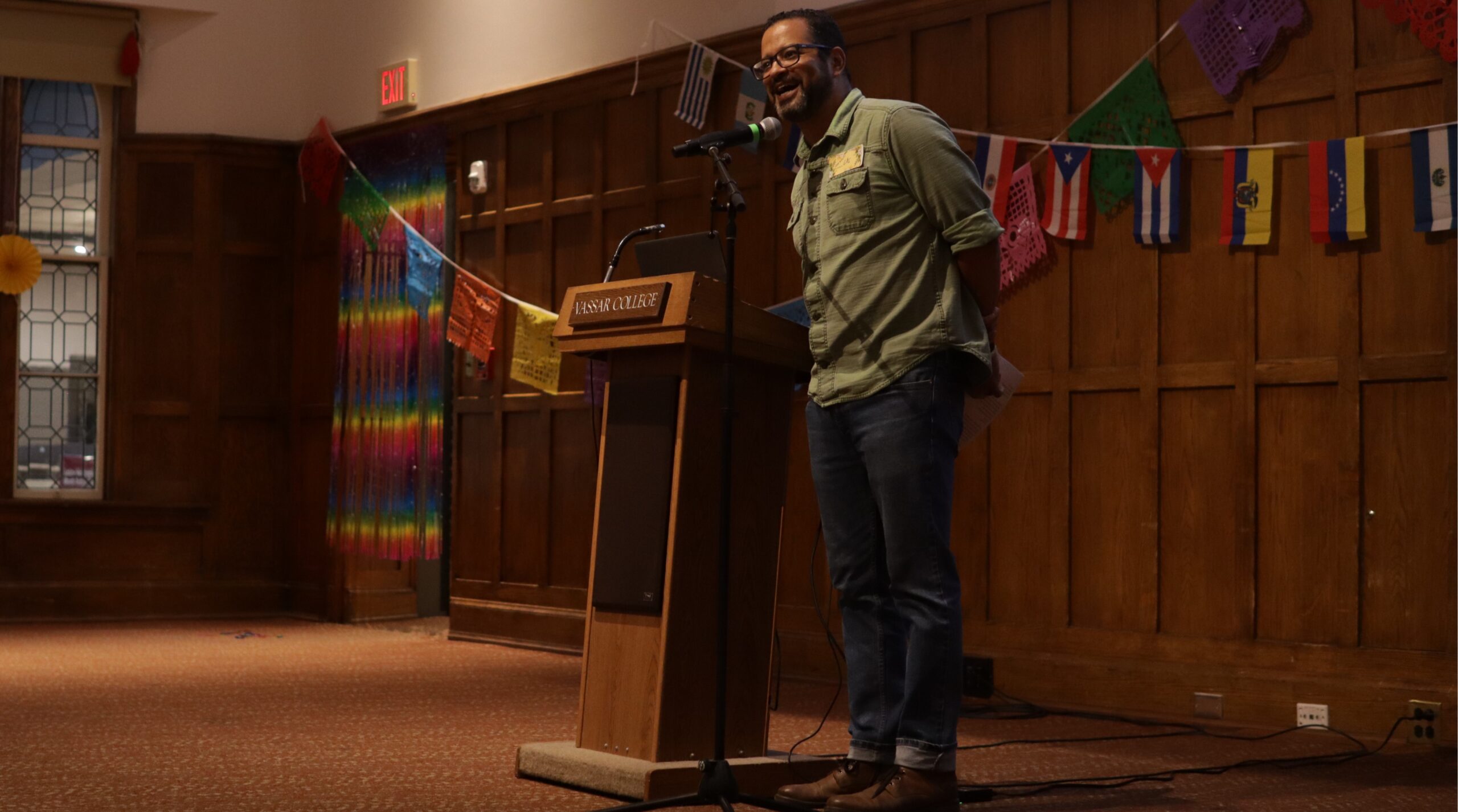 Dean Luis Inoa standing in the center of the stage behind the mic stand, speaking into the mic with his hands positioned behind his back.