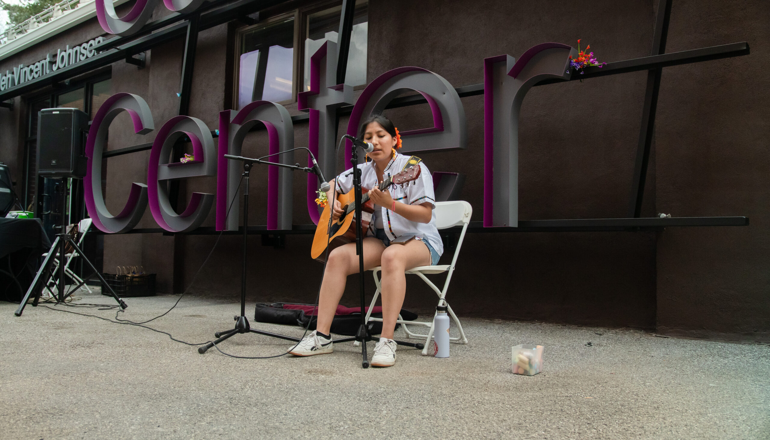 Dariana Reyes Marquez '26 seated in a chair outside the ALANA Center singing into the mic as she plays the guitar.