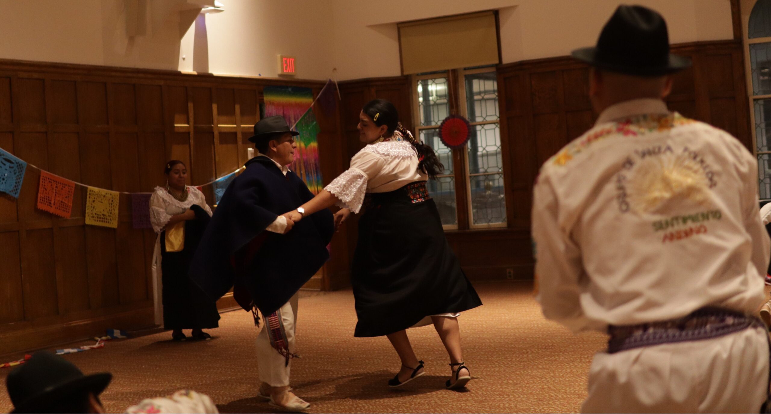 Four members of the dance group are pictured. A couple is dancing in the center, holding hands while the other couple is standing on opposite sides of the performance set. 