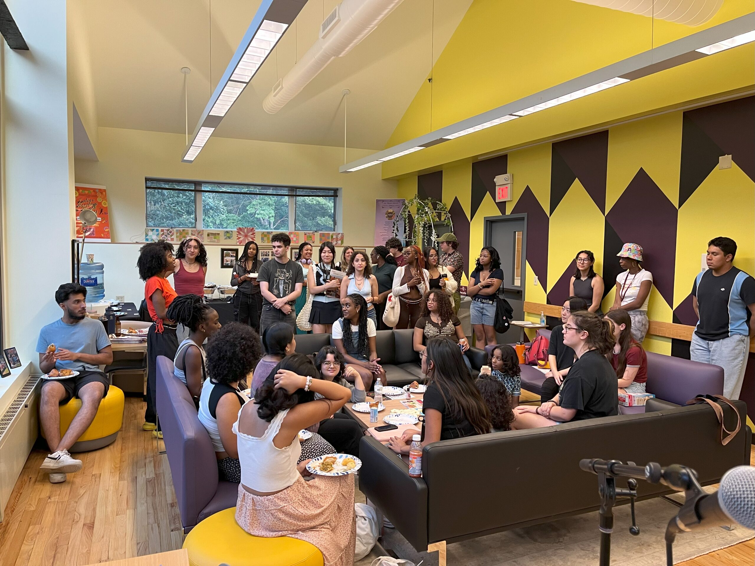 Large number of students seated on sofas/chairs and standing in the community room.