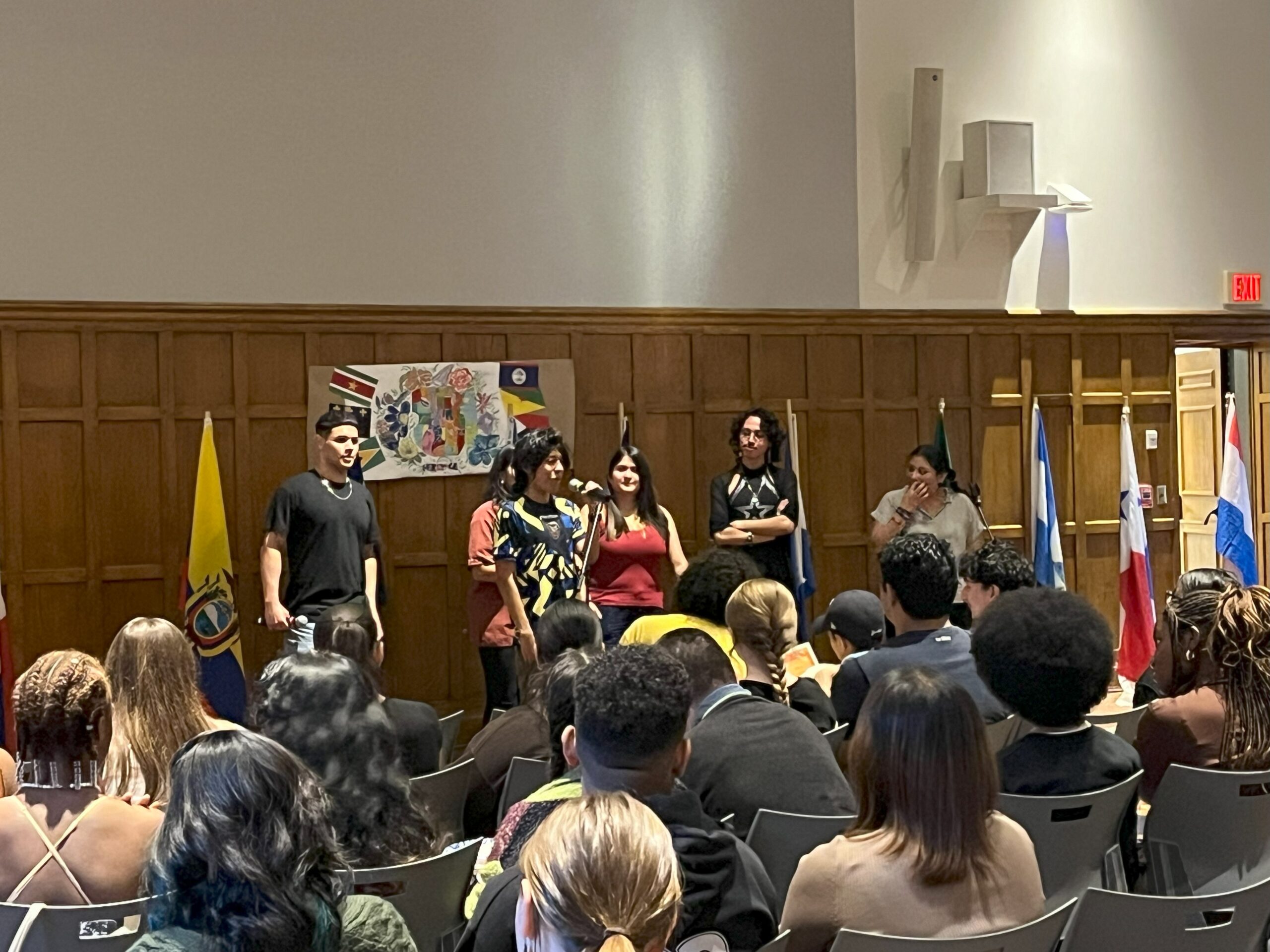 Six members of LSU standing at the center of the stage facing the audience while the audience all seated look on ahead. 