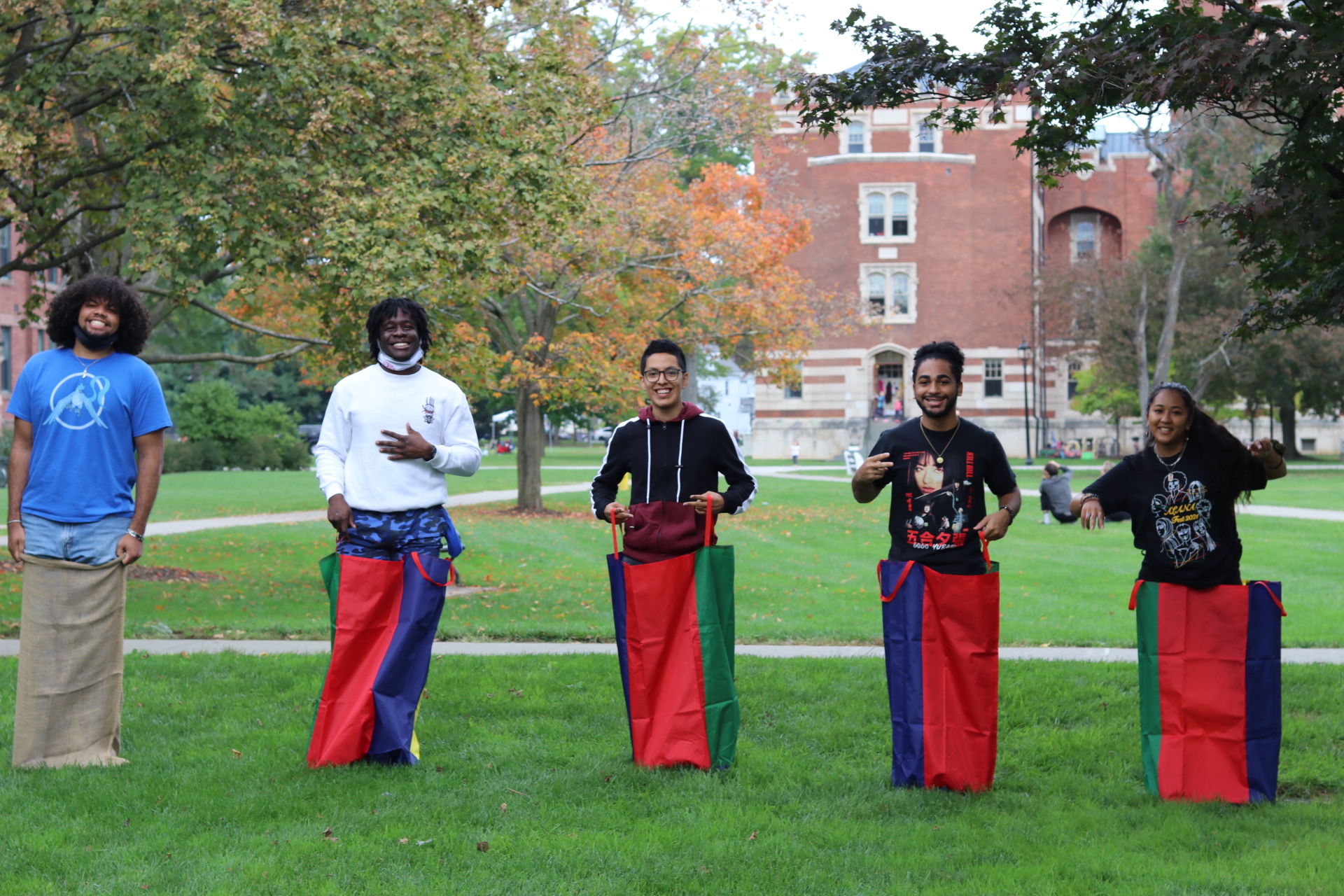Five students standing in sacks side by side on the grass ready to participate in a competition.