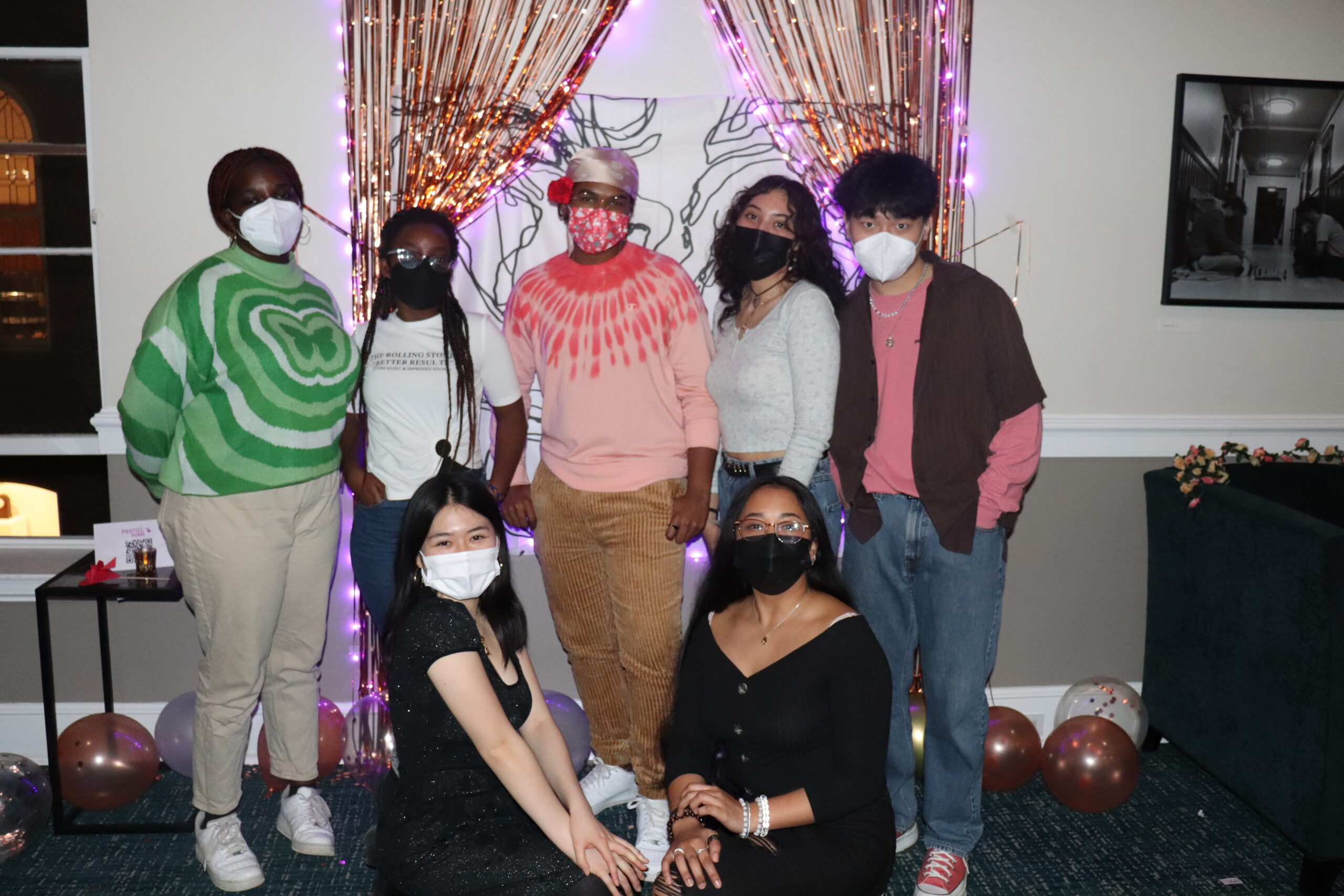 Seven ALANA Interns posing in front of the photo booth. Five students are standing, two are positioned lower creating two rows.