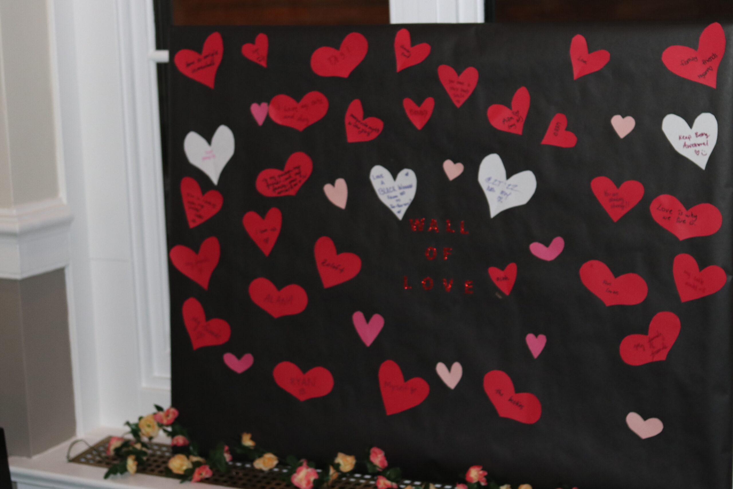 Boad with red, pink and white colored paper hearts with the words "Wall of Love" in the center.