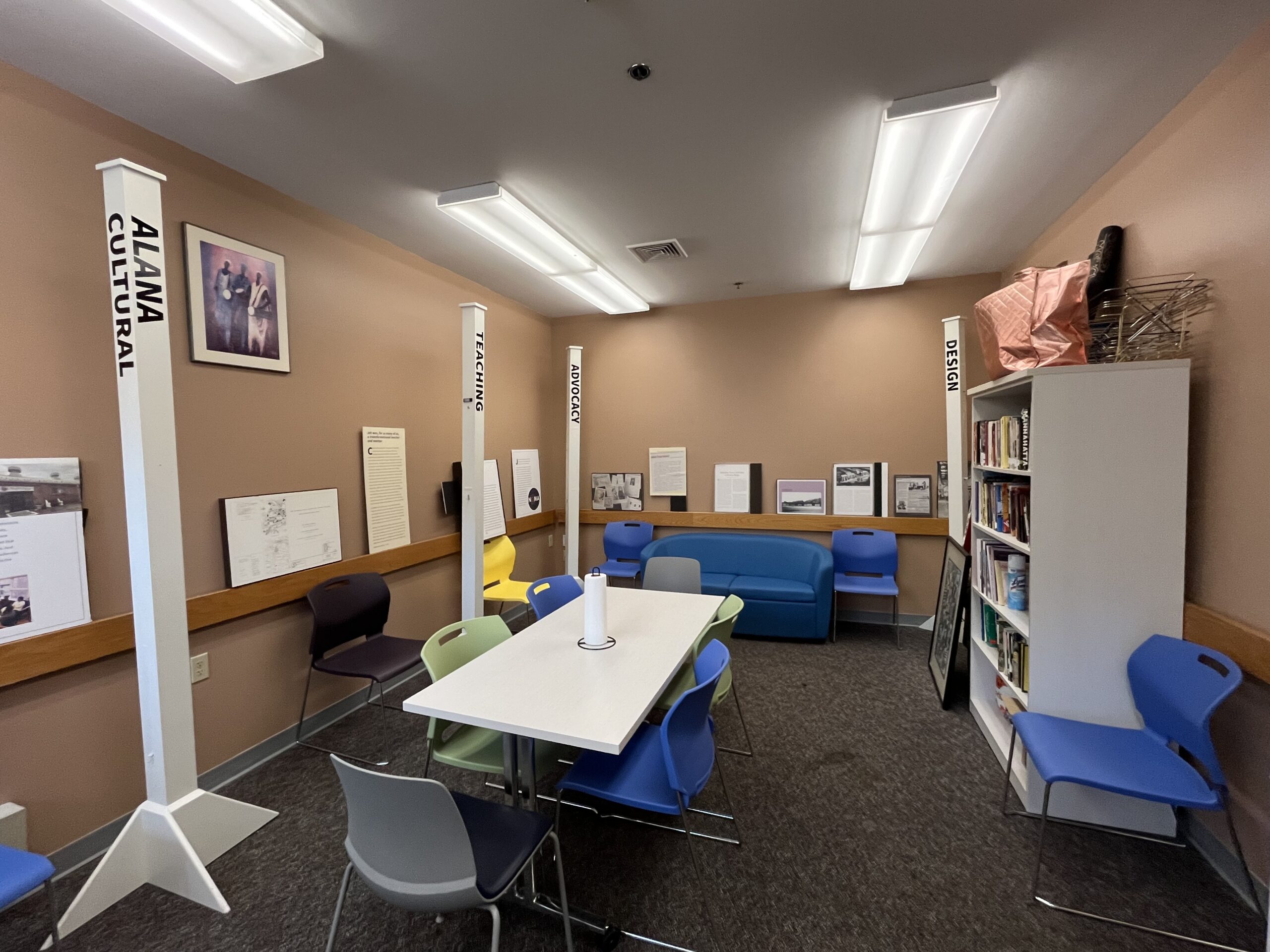 Long gray rectangular table with six chairs around it, a blue sofa, gray bookcase, and blue, purple and yellow chairs places around the room against the walls.