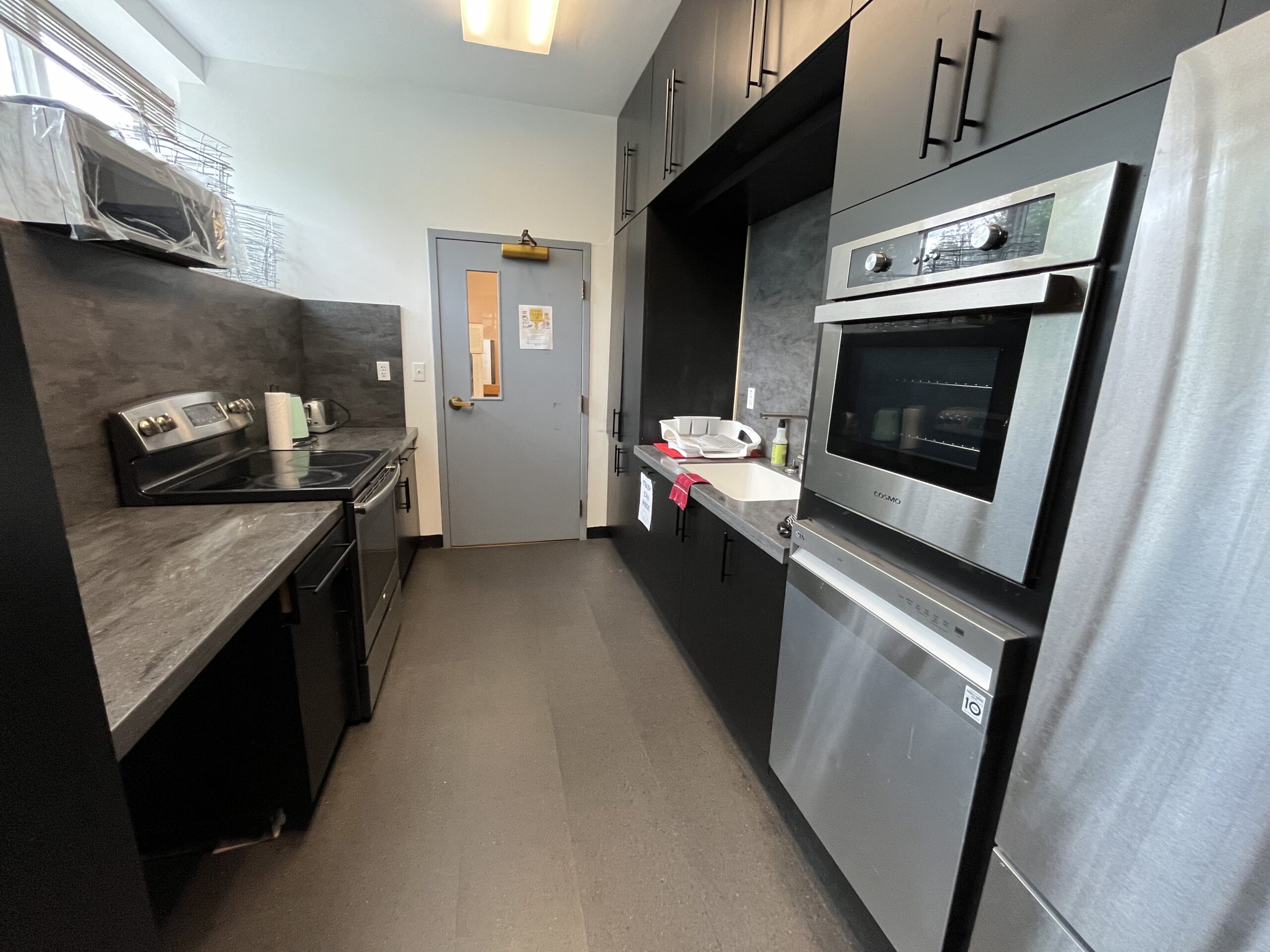 Silver and black metal fridge, dishwasher, stoves with all black cabinets, marbel counter space and blue door.