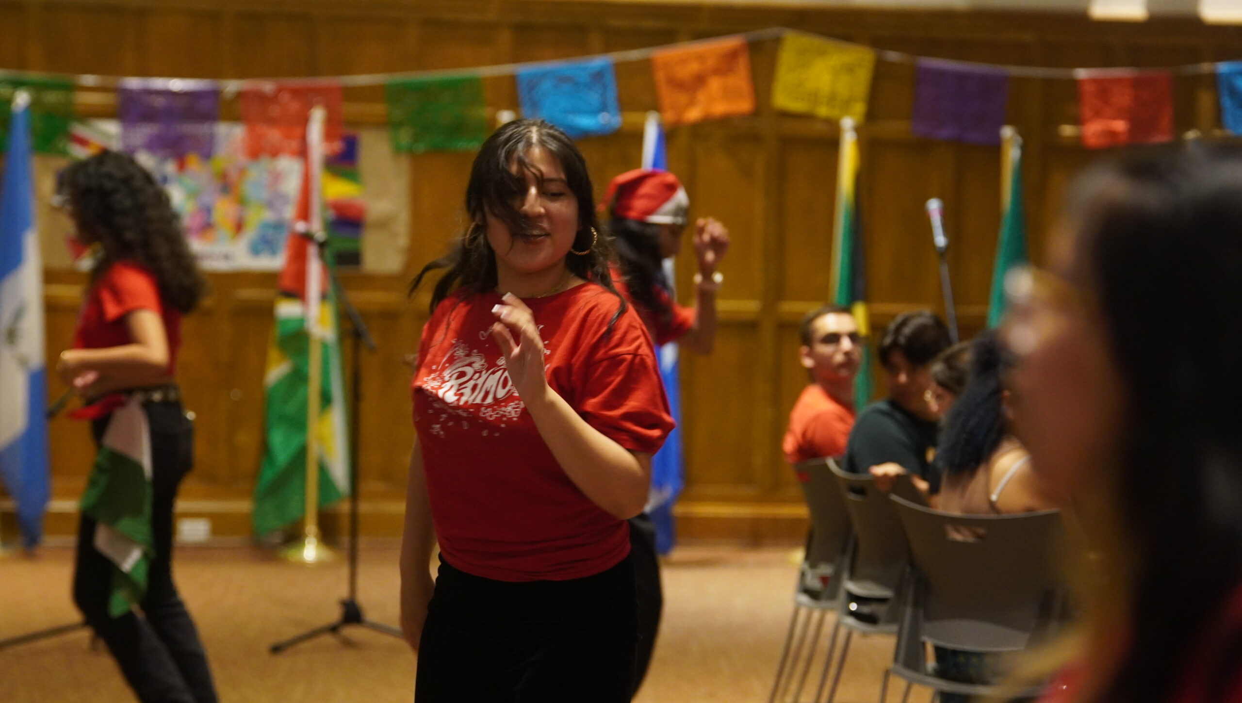 Students leaders from Ritmo dancing with their arms up at their sides, wearing red shirts and black pants.