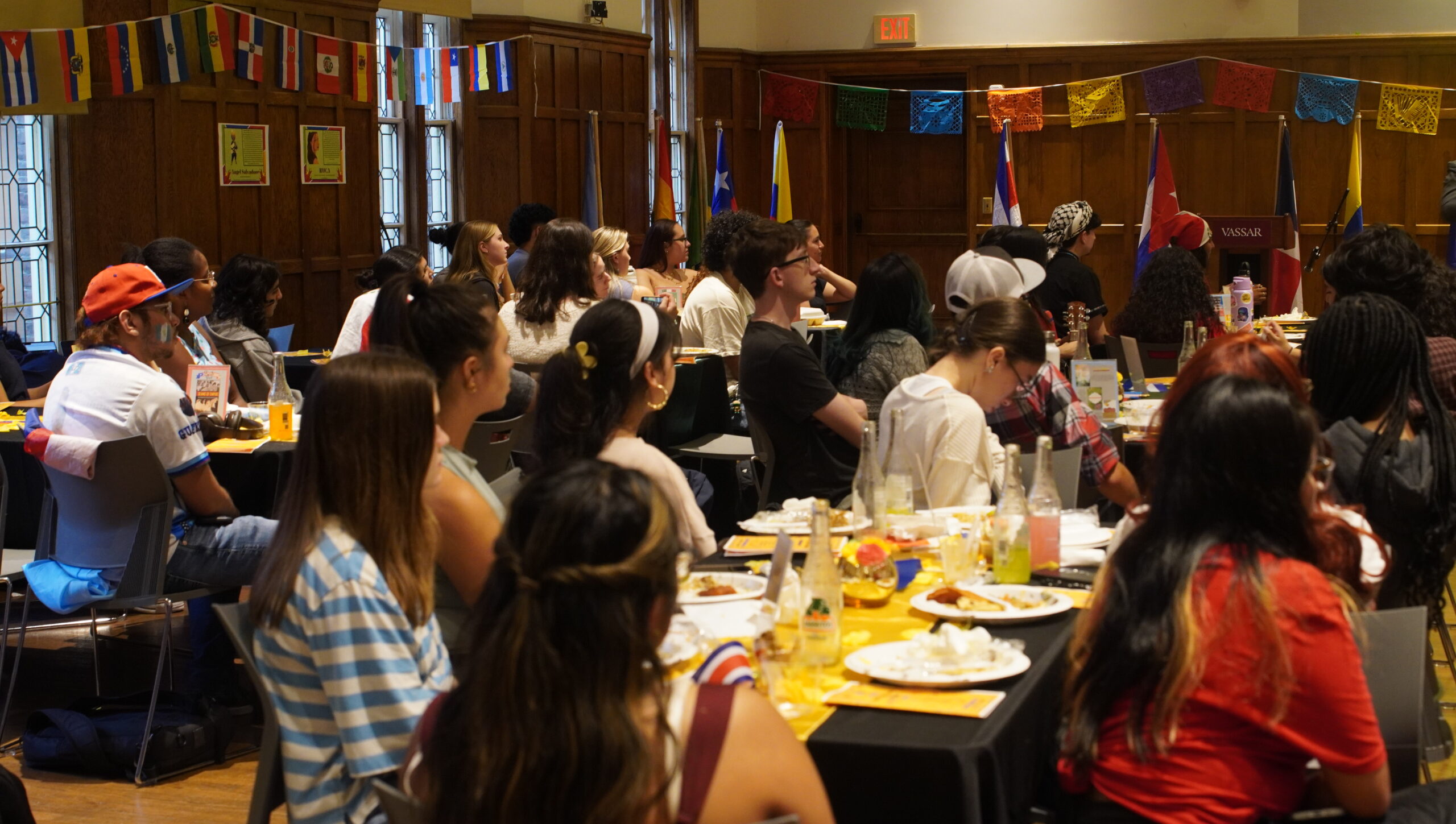 Back facing photo of large group of students seated with their attention to the front of the stage.