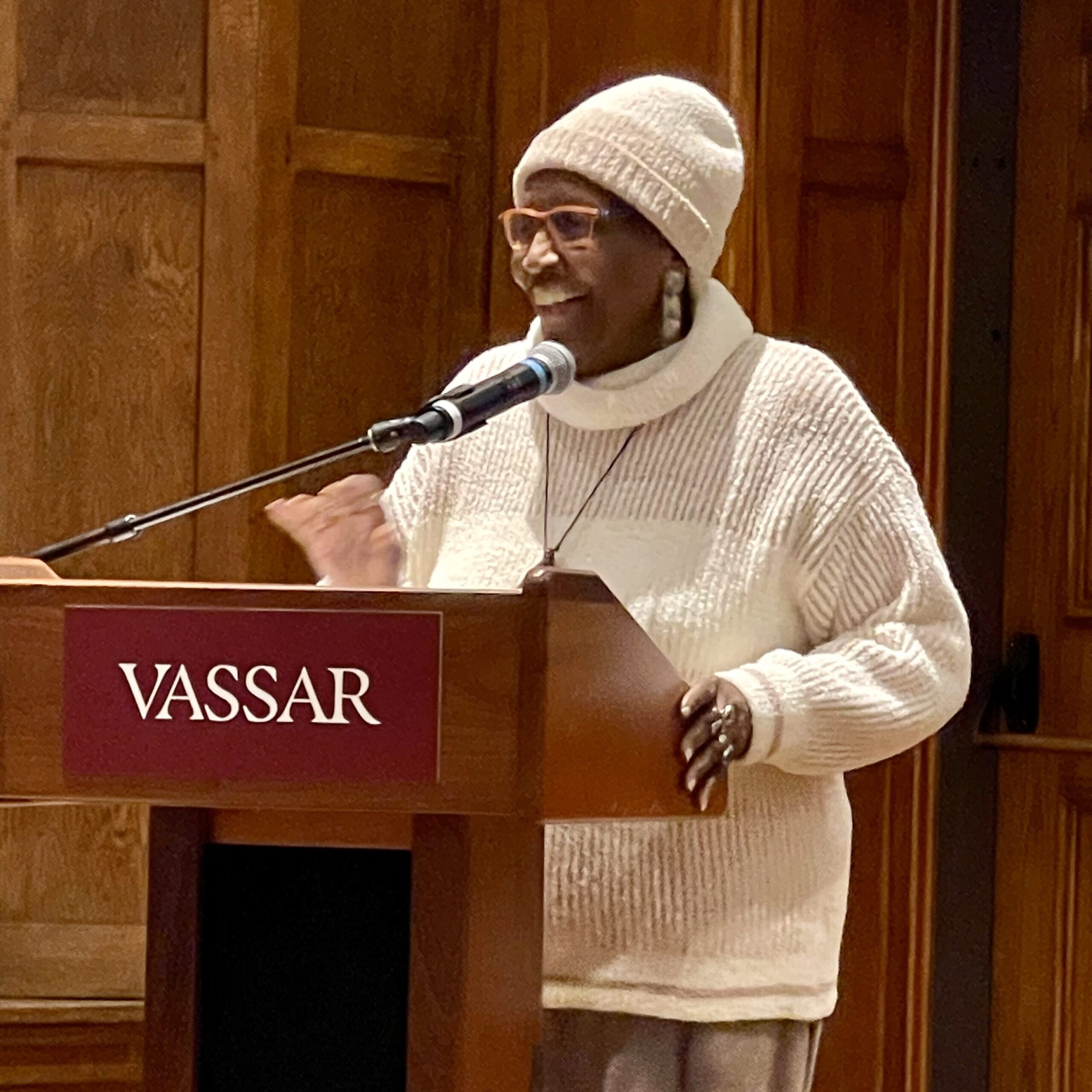 Community speaker Miss Carmen standing at the podium with her left hand on the podium side and her right hand slightly elevated as she speaks.