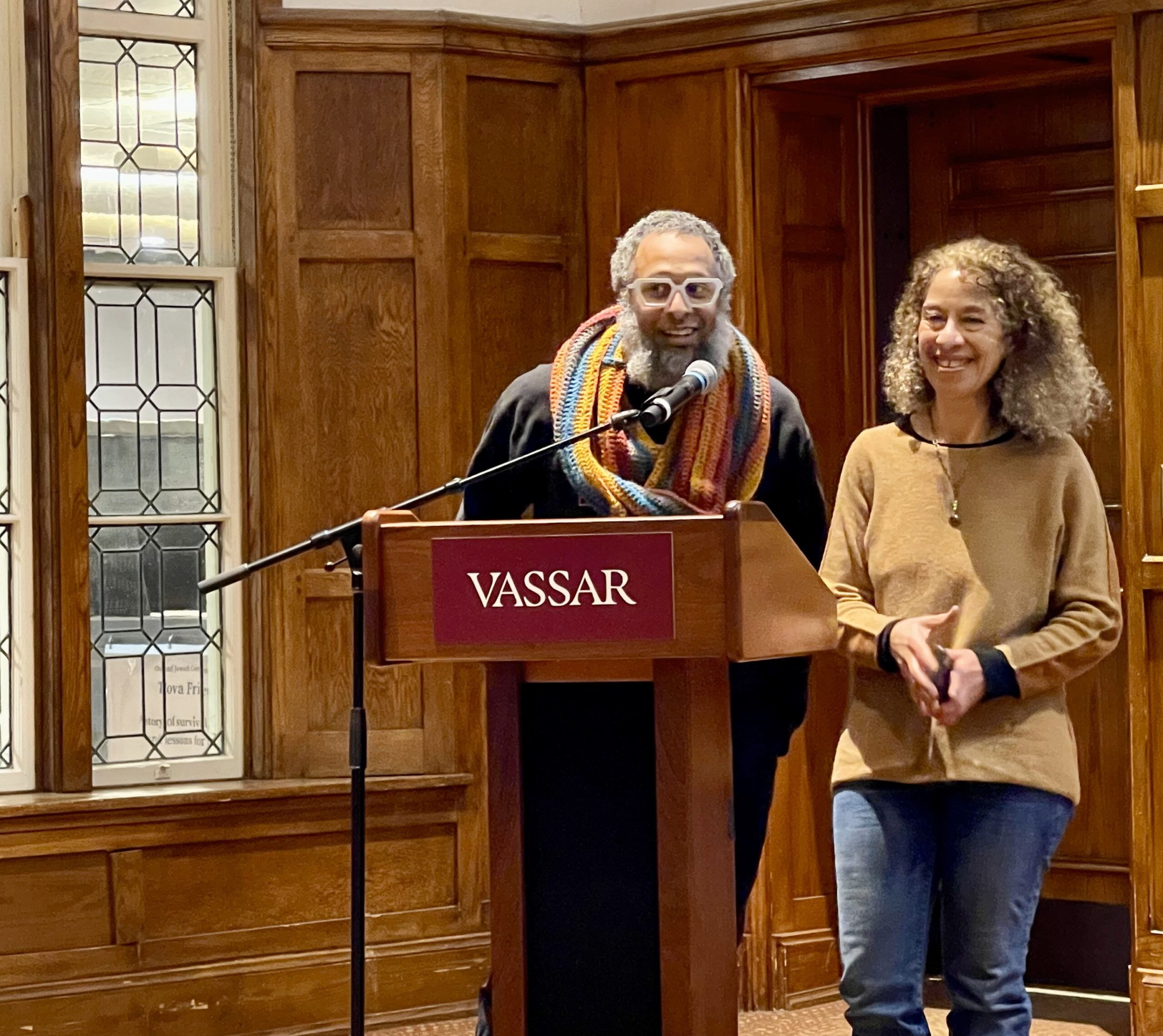 Micah and Dara standing side by side behind the podium. Micah is speaking into the mic as Dara smiles with her hands together.