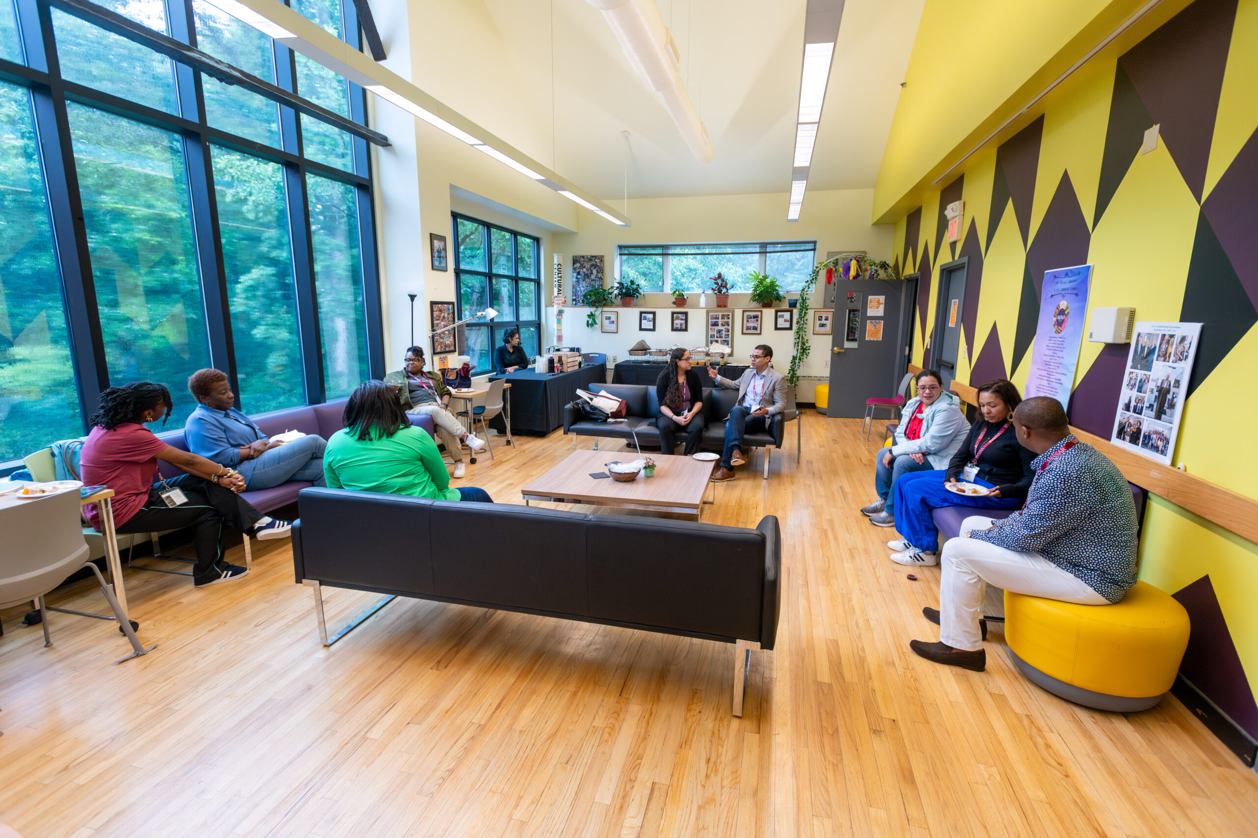 A wide shot of the ALANA Center community room with people seated along the sides of the room around the space.