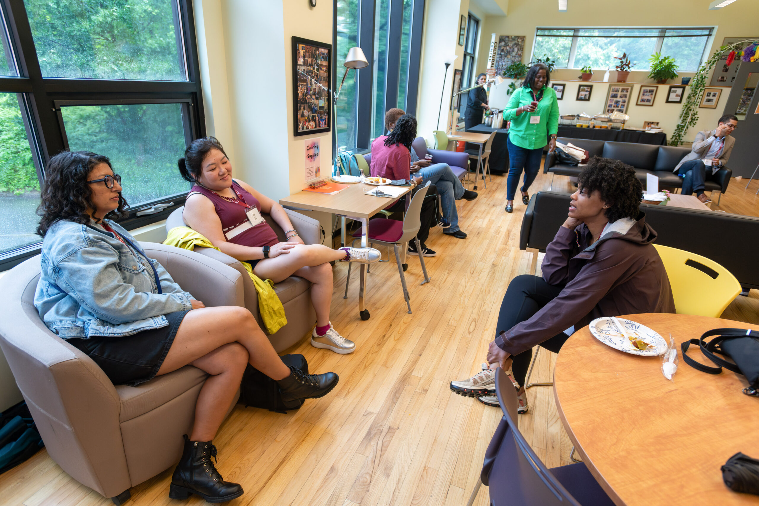 A group of three alums gathered together. Two alums are seated to the left in front of the window as one alum sits across in a yellow chair. 
