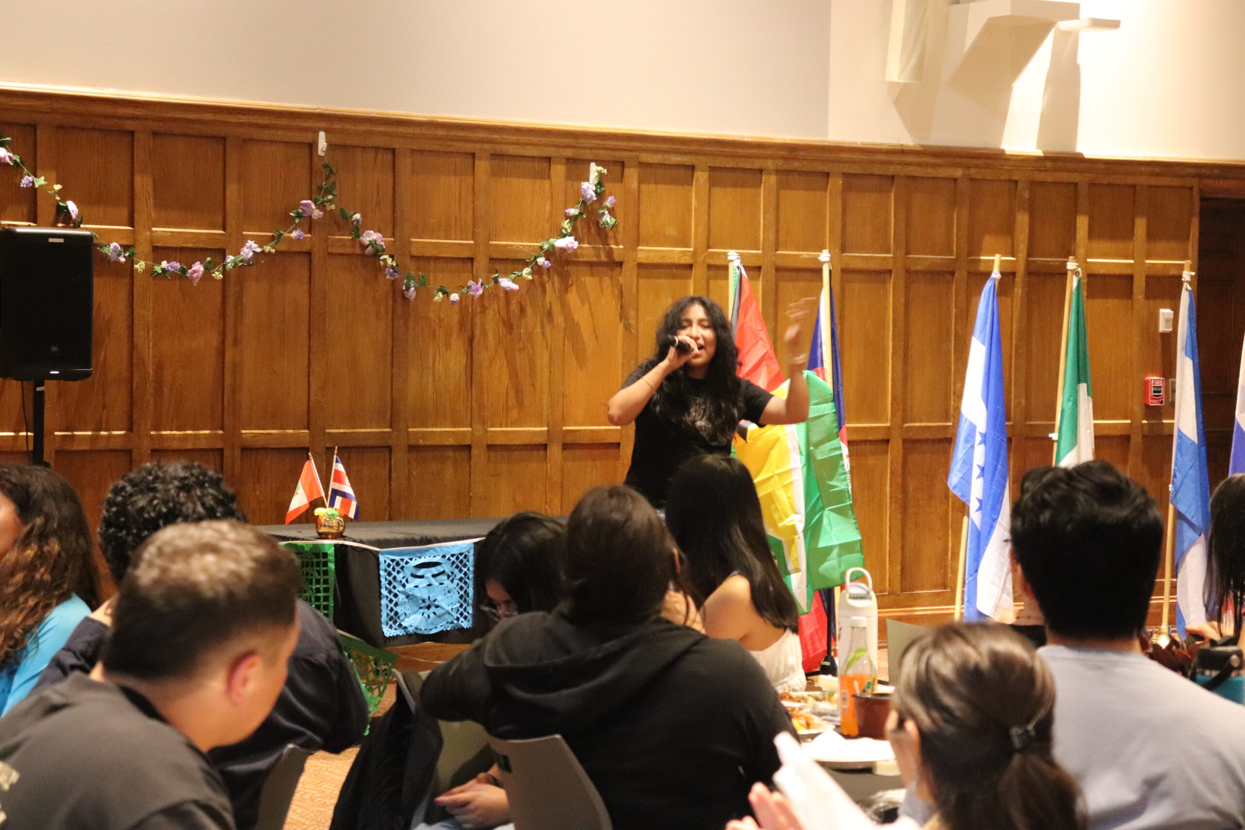 Performer singing into the mic with her left hand in the air as her right hand hold the mic