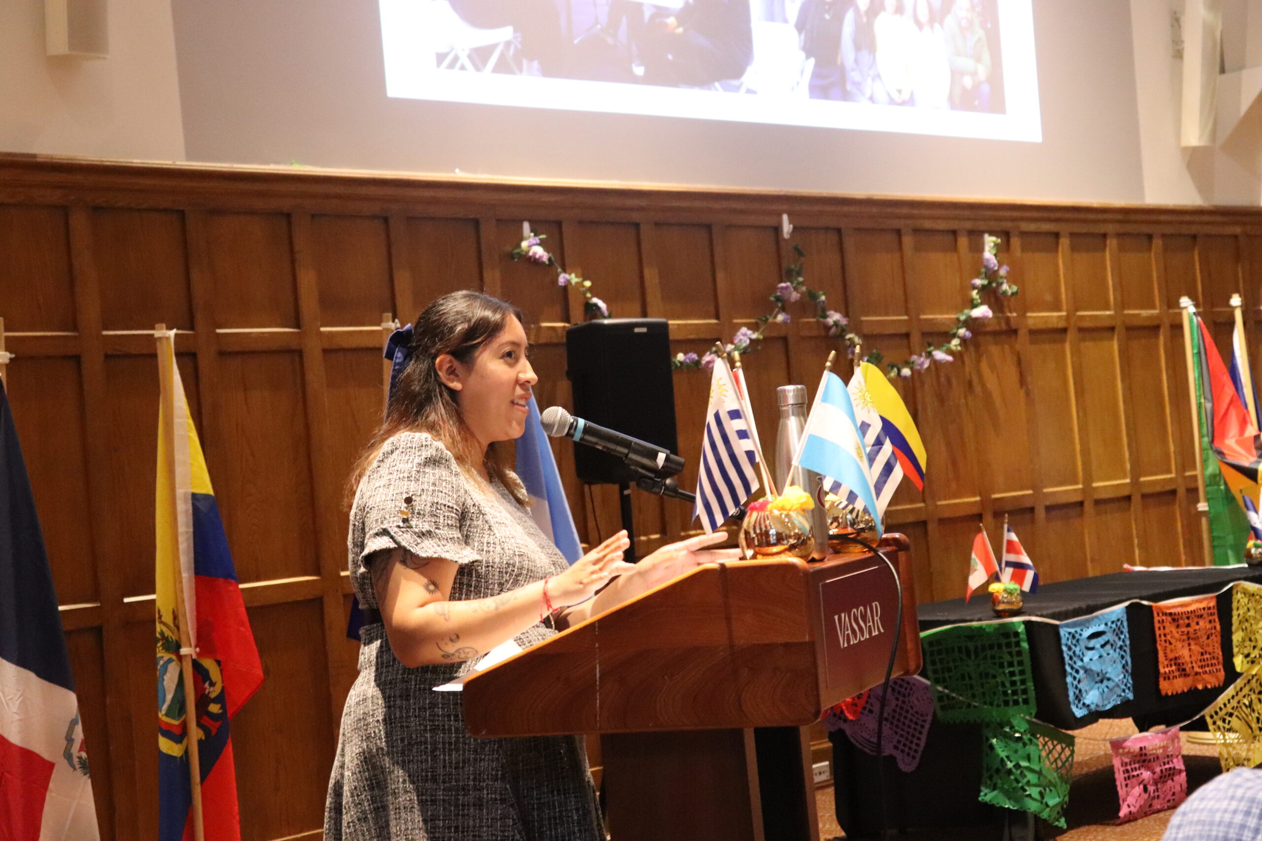 Speaker standing at the podium speaking into the mic as she looks into the audience with her hands slightly lifted