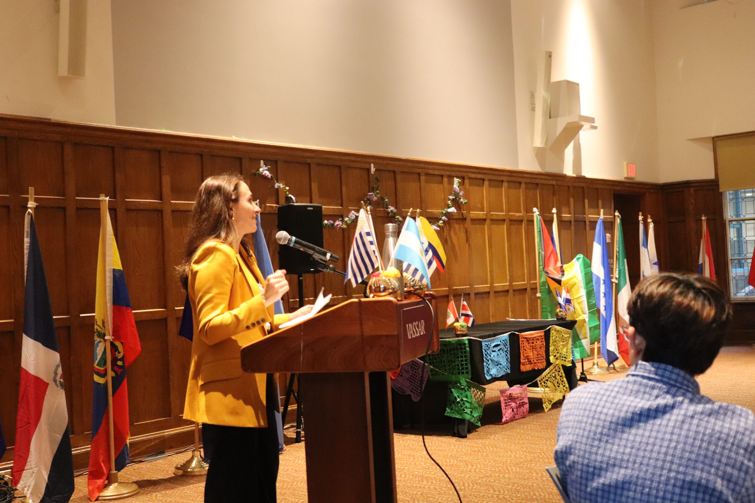 Speaker wearing a yellow blazer standing at the podium speaking into the mic