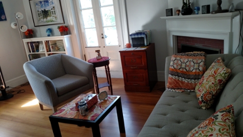 A room with a couch and chair set up across from each other with natural light coming through a large window.