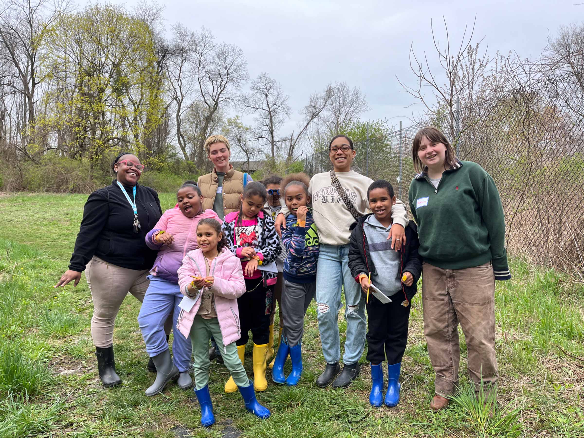 A group of children and young adults stand in a field at the Vassar Ecological Preserve.