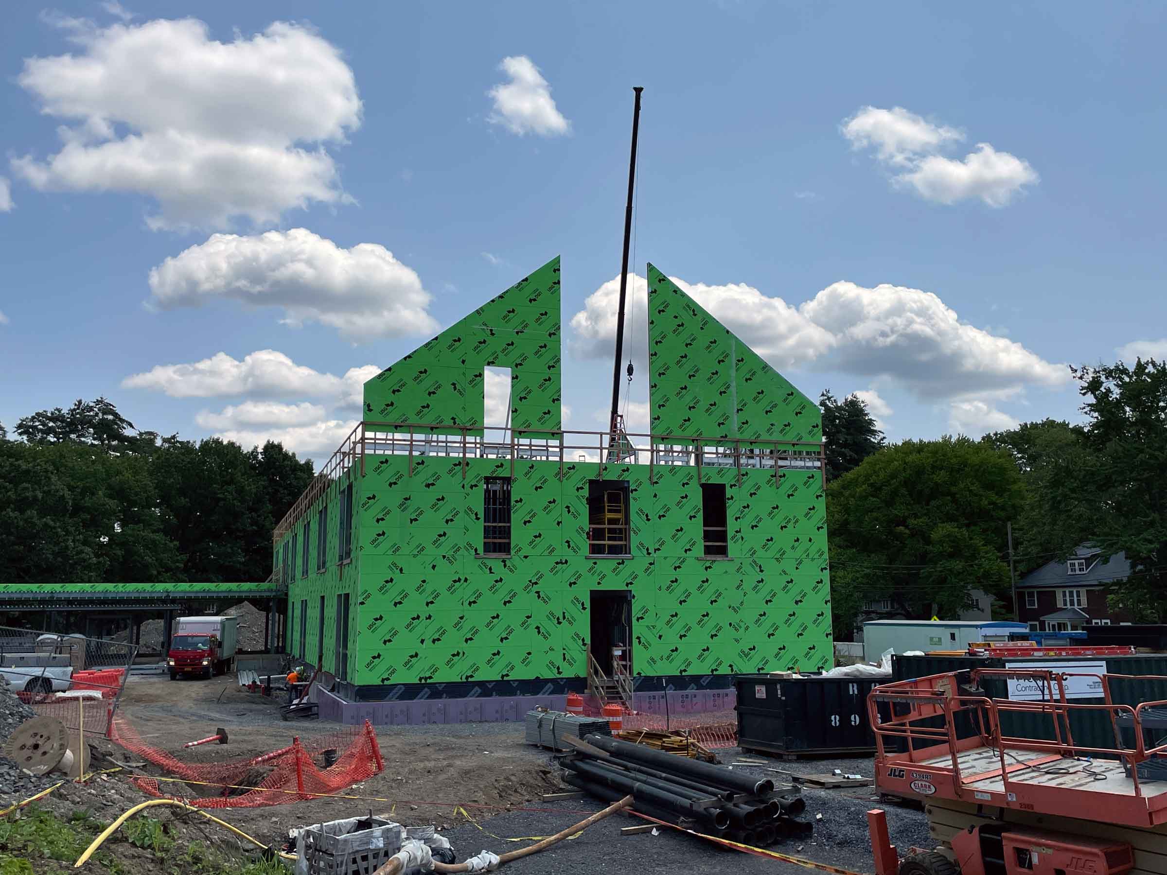 building in process of being constructed with green paneling and a crane behind