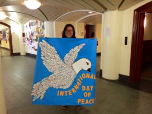 Woman holding up a banner of a dove with words "International Day of Peace".
