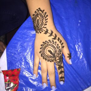 Person's hand on top of blue plastic with light purple nail polish and an intricate henna design on the hand and some arm.