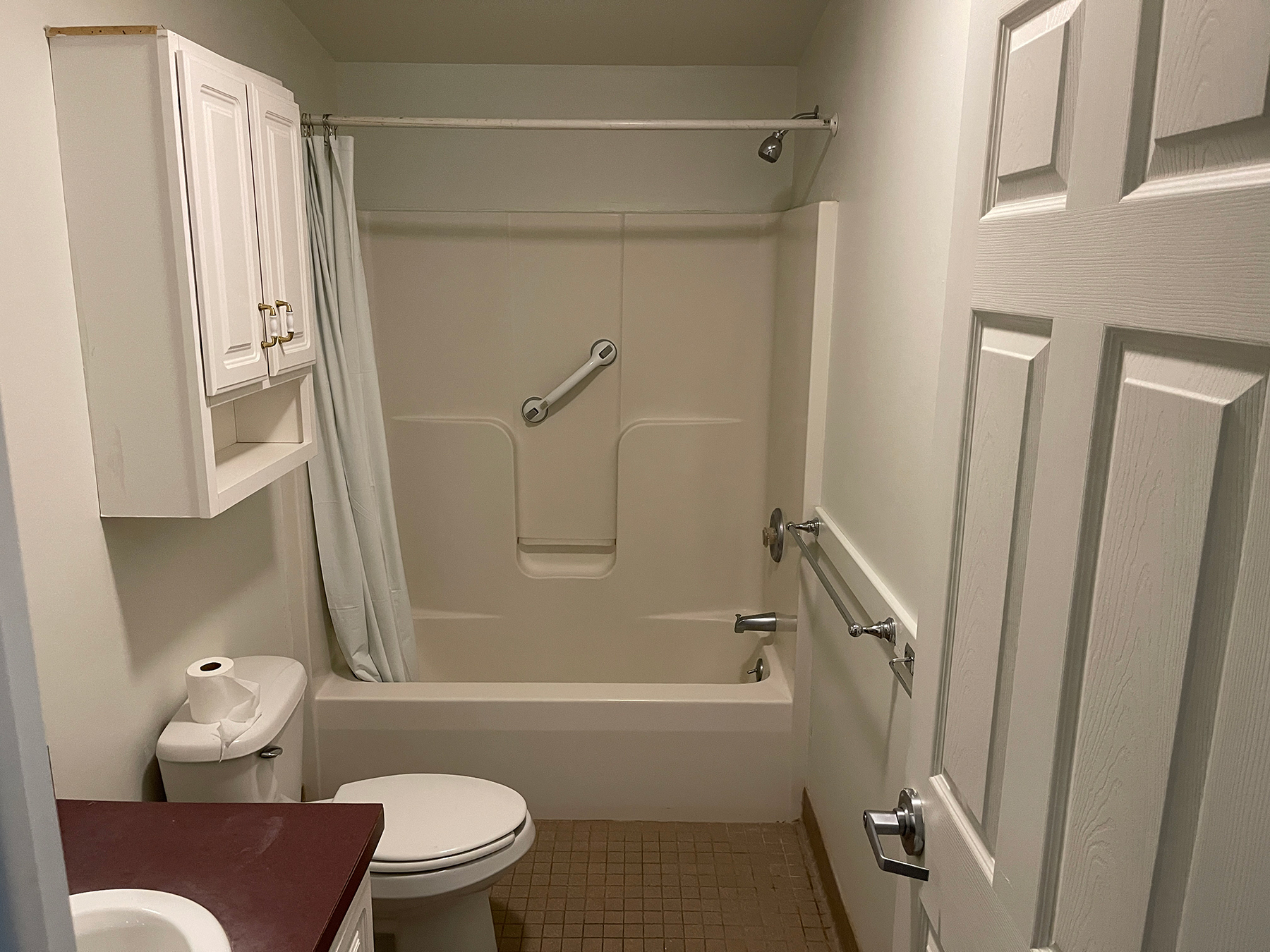 Bathroom with a sink, toilet, white cabinet above the toilet, tub, and shower.