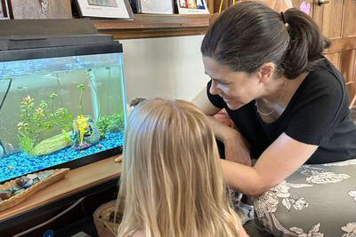 Adult and small child looking at a fish tank on a wooden surface in a room.